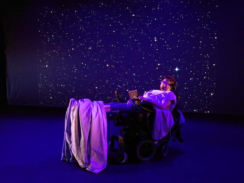 The background is dark blue with stars. In the foreground is a person in a hospital bed.